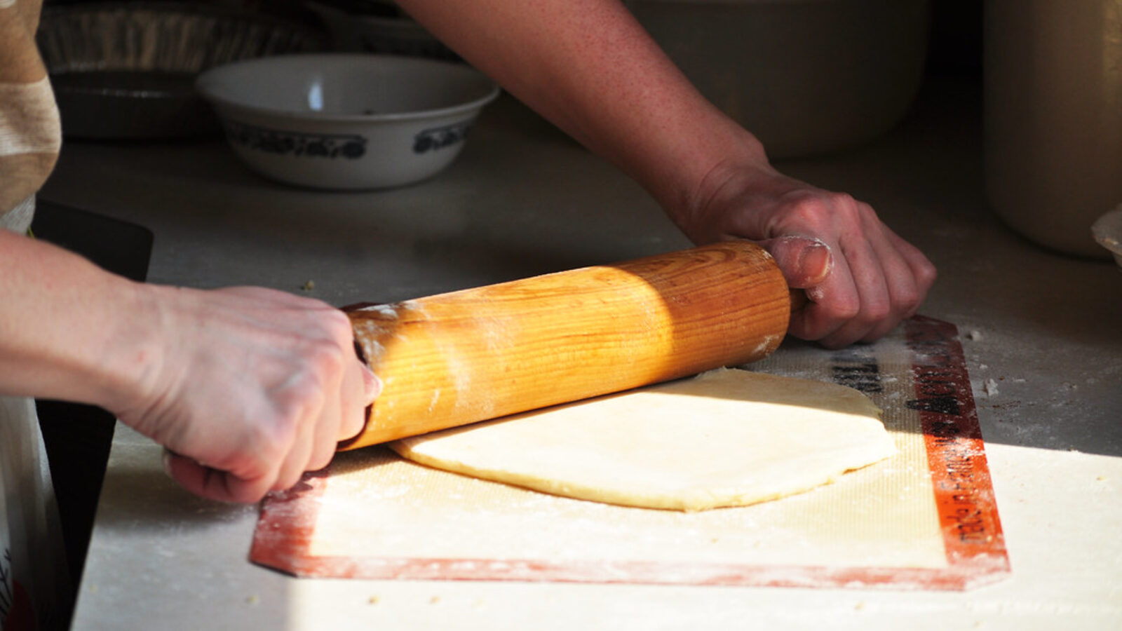 Hands rolling out pastry with a wooden rolling pin